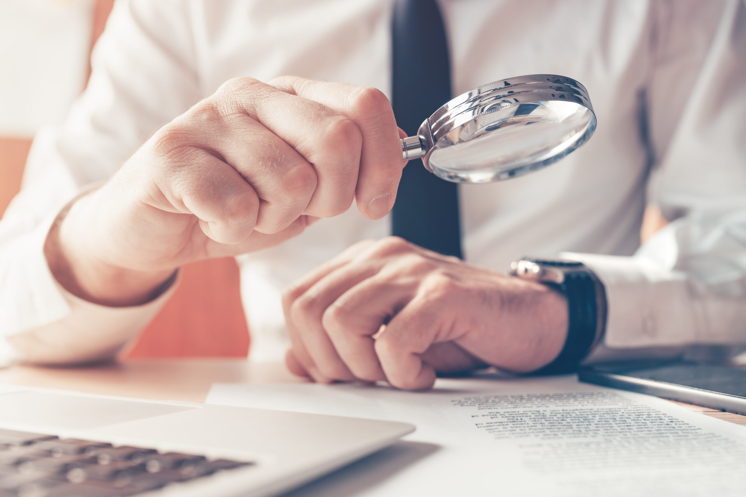 Cautious businessman reading contract agreement with magnifying glass, close up with selective focus